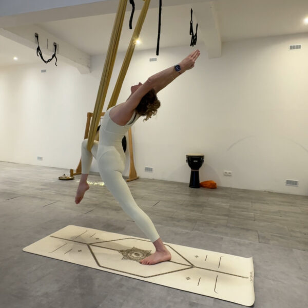 Virginie en fente arrière, un pied dans le hamac de yoga aérien, bras tendus vers l'avant, cours de yoga flow aérien à Chamonix