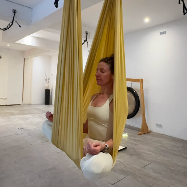 Virginie assise en tailleur dans le hamac de yoga aérien, yeux fermés, cours de yoga aérien restauratif à Chamonix