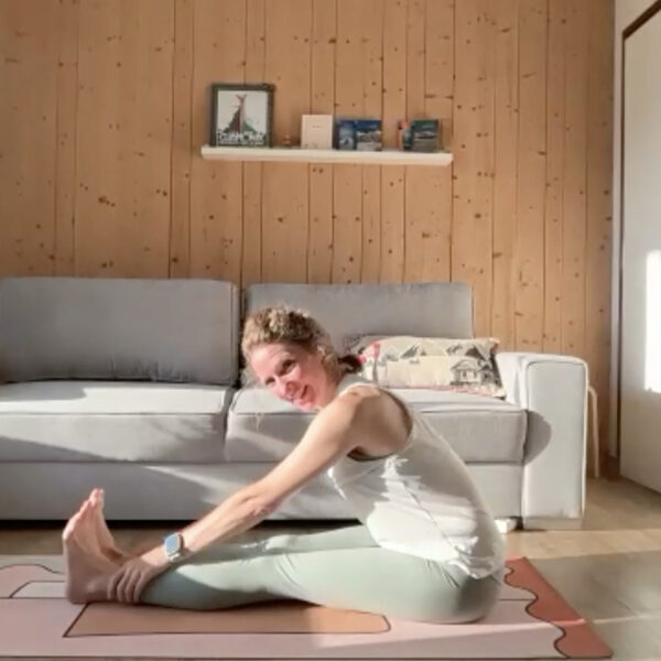 Virginie Gosselin en pince assise (Paschimottanasana) sur son tapis, cours de yoga du matin en ligne