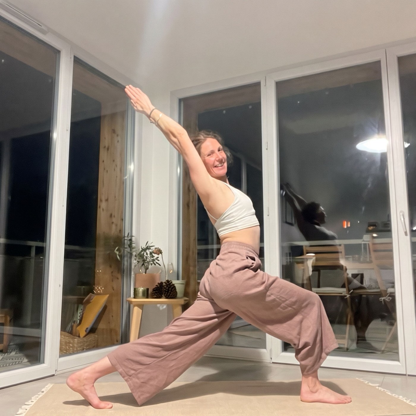 Virginie en grand croissant de lune (Ashta Chandrasana), bras tendus, pendant un cours de yoga vinyasa en ligne, chez elle le soir